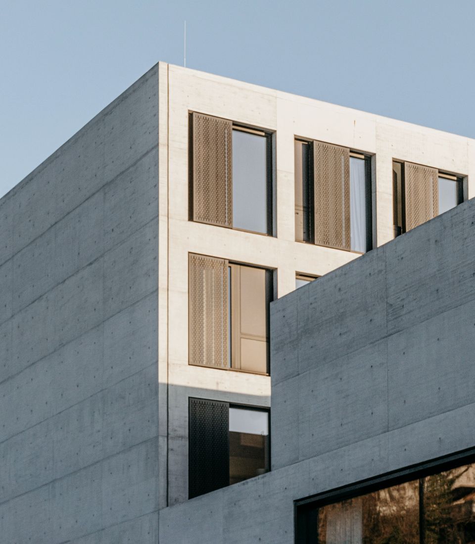 Corner of a concrete building with tall shuttered windows catching low afternoon light